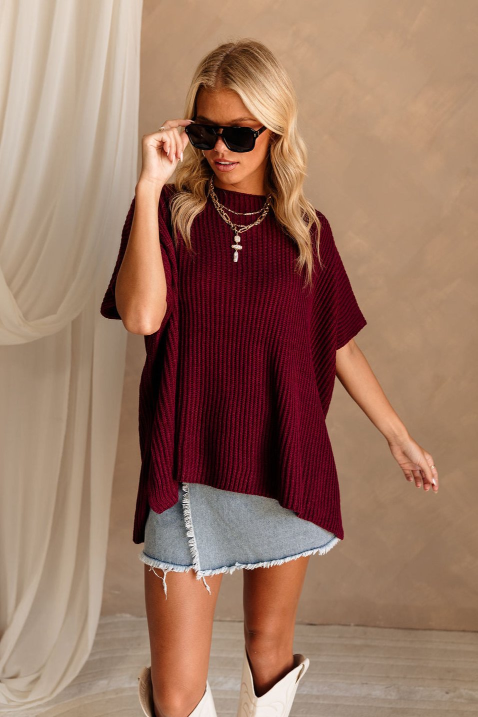 Front view of female model wearing the Heather Oversized Sweater in Maroon, which has a round neck, side slits, and short poncho sleeves. 