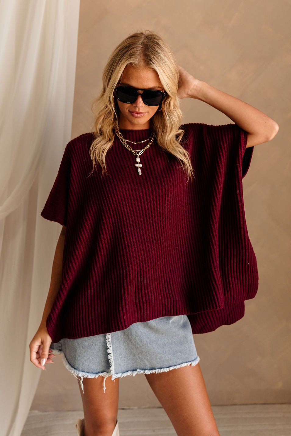 Front view of female model wearing the Heather Oversized Sweater in Maroon, which has a round neck, side slits, and short poncho sleeves. 