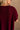 Close back view of female model wearing the Heather Oversized Sweater in Maroon, which has a round neck, side slits, and short poncho sleeves. 