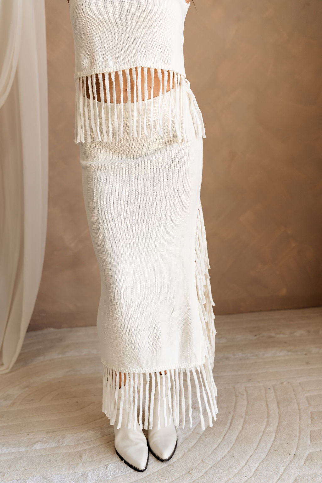 Lower body front view of female model wearing the Hillary Ivory Fringe Midi Skirt, paired with matching top.