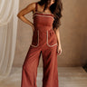 Full body front view of female model wearing the Carmella Rust Wide Leg Jumpsuit that has rust fabric, crochet trim, and wide legs.