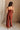 Full body back view of female model wearing the Carmella Rust Wide Leg Jumpsuit that has rust fabric, crochet trim, and wide legs.