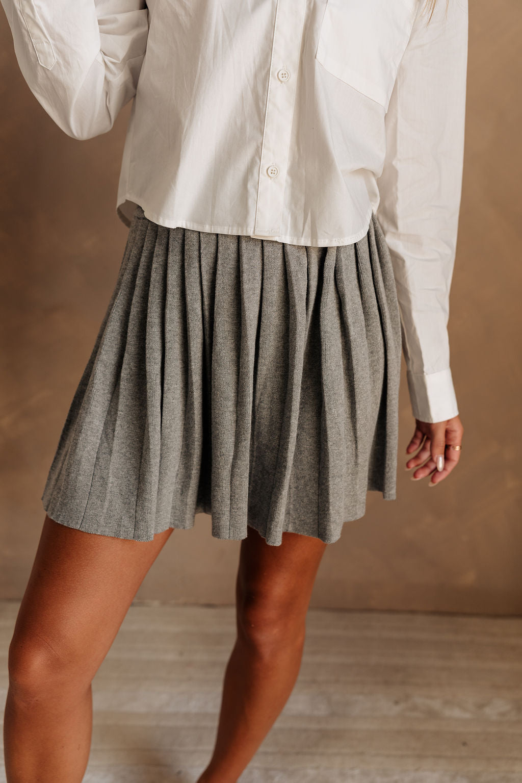 Close up front view of female model wearing the Misha Grey Pleated Mini Skirt that has grey sweater fabric and pleating. Worn with white top.