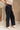 Lower body side view of female model wearing the Wyatt Black Denim Braided Jeans that have washed black denim, wide legs, and a braided waistband. Worn with beige top.