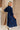 Full body back view of female model wearing the Penny Button Up 3/4 Sleeve Midi Dress in Navy that has a button up front, 3/4 sleeves, and a collar.