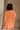 Back view of female model wearing the Heather Oversized Sweater in Orange, which has a round neck, side slits, and short poncho sleeves. 