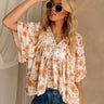 Front view of female model wearing the Milly Cream & Orange Floral Top that has a buttoned v-neck, lace trim, and short sleeves.