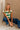 Full body view of female model wearing tStacia Green & White Striped Sweater Tank, worn with jeans; model shown squatting.
