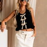 Front view of female model wearing the Sasha Black Bow Sweater Tank, paired with a white skirt.