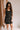 Front view of female model wearing the Peyton Denim Zip Front Mini Dress in black, that has washed black denim fabric, a gold front zipper, straps with buckle adjustments, and pockets.