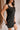 Close-up side view of female model wearing the Peyton Denim Zip Front Mini Dress in black, that has washed black denim fabric, a gold front zipper, straps with buckle adjustments, and pockets.
