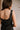 Close upper back view of female model wearing the Peyton Denim Zip Front Mini Dress in black, that has washed black denim fabric, a gold front zipper, straps with buckle adjustments, and pockets.