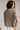back  view of female model wearing the Ramsey Mocha Short Sleeve Top that has knit fabric, a mock neck, a front chest pocket, and short sleeves