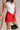 Front view of female model wearing the Rhiannon Frayed Tank that has white fabric and a frayed hem. Worn with red mini skirt