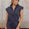 Upper body front view of female model wearing the Alli Charcoal Zip-Up Romper that has dark gray fabric, a collar, and a zip front. 