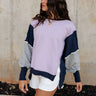 Front view of female model wearing the Lucia Color Block Sweatshirt that has purple, navy, and grey color blocking. Worn with white shorts.