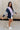 Full body side view of female model wearing the Lucia Color Block Sweatshirt that has purple, navy, and grey color blocking. Worn with white shorts.