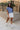 Full body front view of female model wearing the Leah Blue Short Sleeve T-Shirt, paired with white shorts.