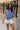 Upper body front view of female model wearing the Leah Blue Short Sleeve T-Shirt, paired with white shorts.