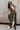 Full body side view of female model wearing the Kimberly Olive Green Jumpsuit, worn over a white shirt.