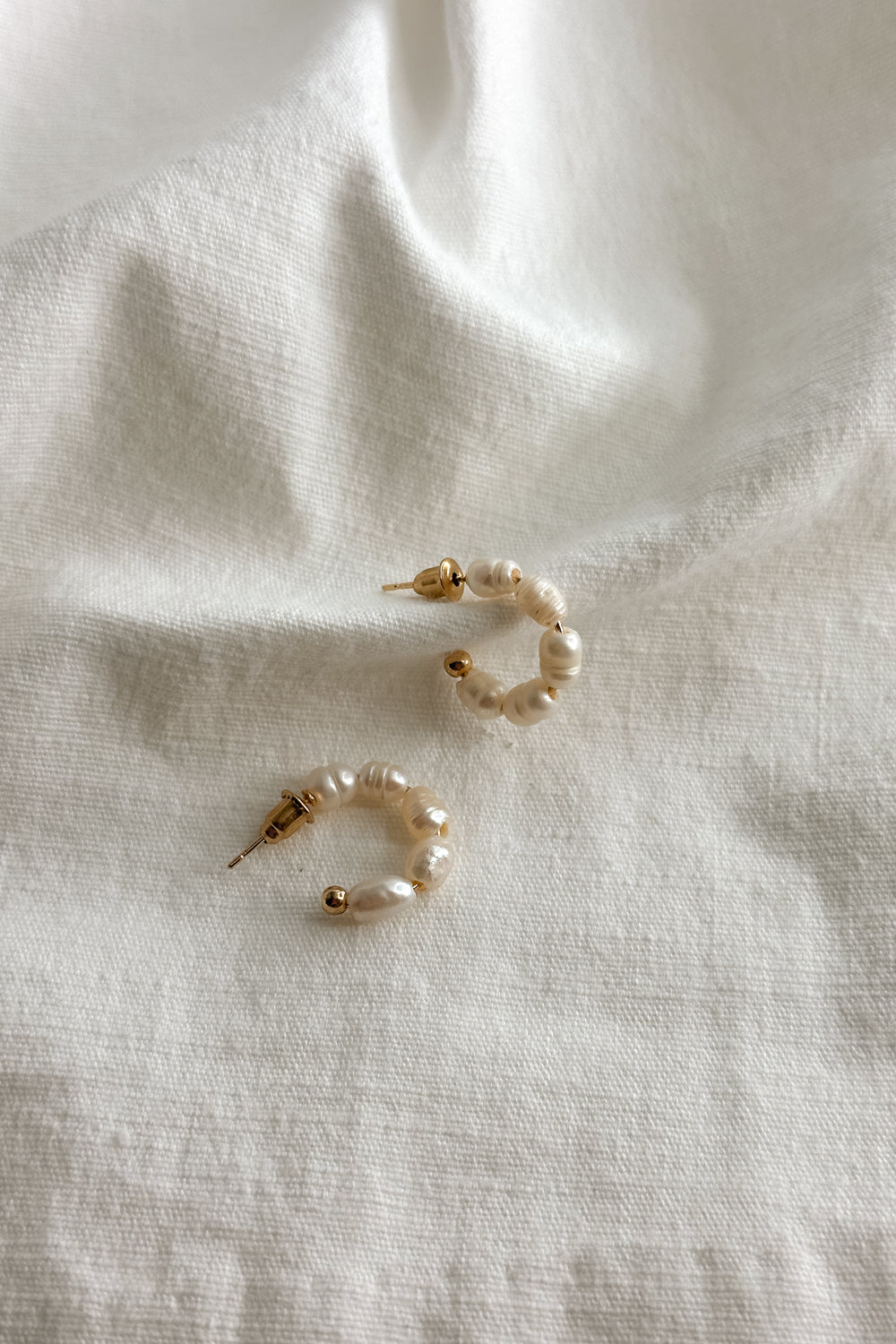 Flat lay view of the Meadow Mini Pearl Hoop Earring which features mini, open gold hoops with pearls
