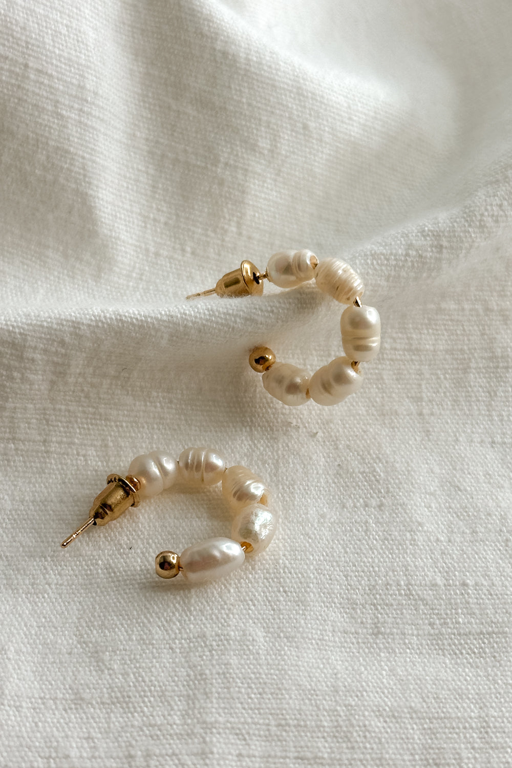 Flat lay view of the Meadow Mini Pearl Hoop Earring which features  mini, open gold hoops with pearls 