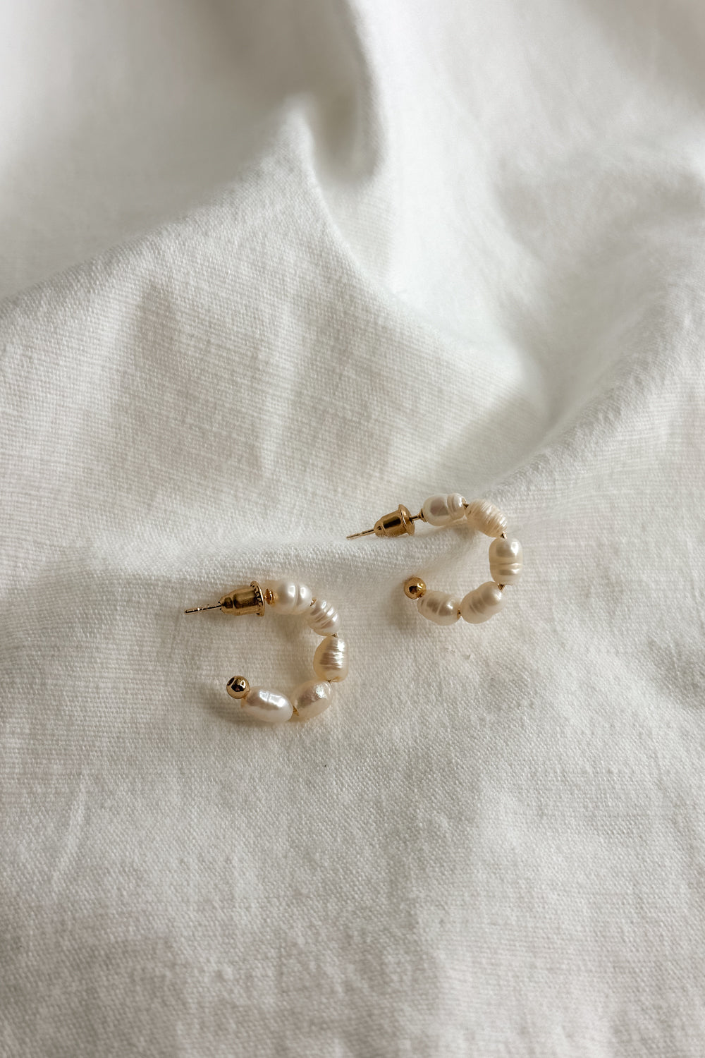 Flat lay view of the Meadow Mini Pearl Hoop Earring which features mini, open gold hoops with pearls