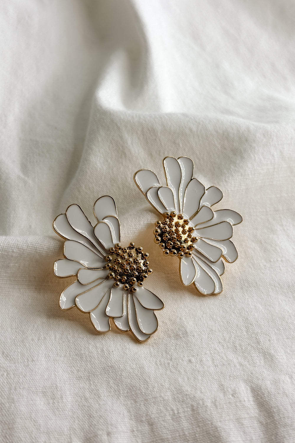 Flat lay view of the Chloe White & Gold Flower Stud Earring which features  oversized white flower studs with gold details