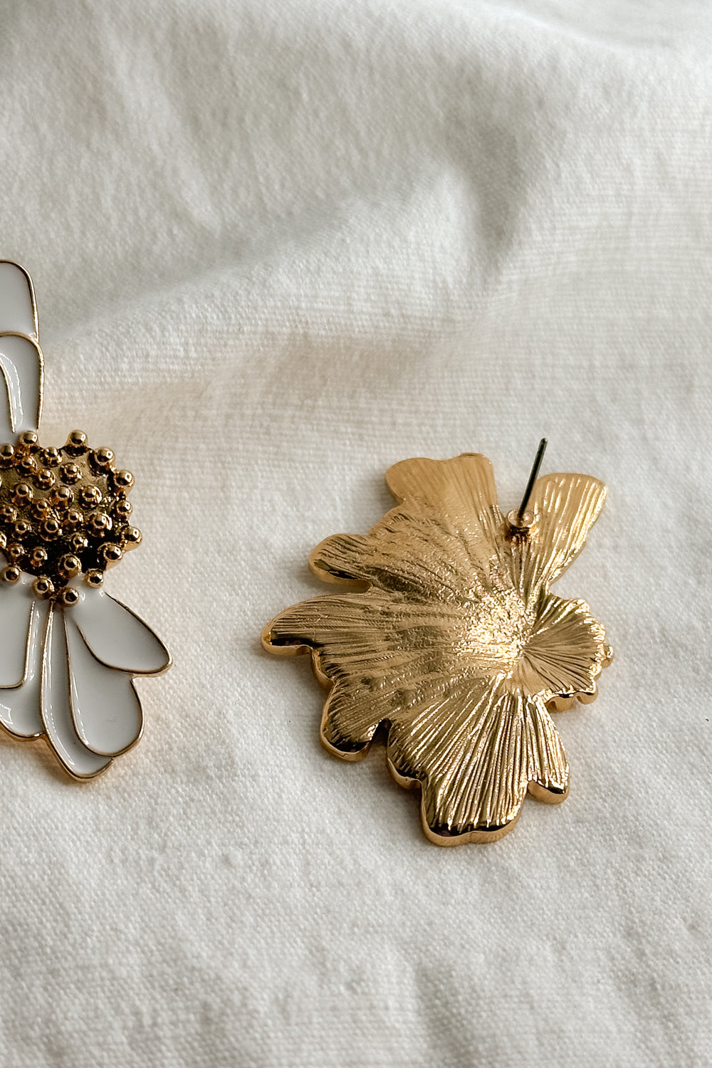 Flat lay view of the Chloe White & Gold Flower Stud Earring which features oversized white flower studs with gold details