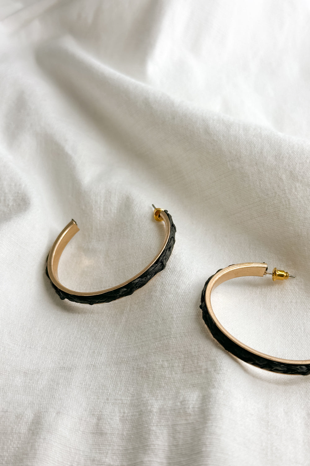 Close up flat lay view of the Jackie Gold & Black Woven Hoop Earring which features open, large gold hoops with black woven details