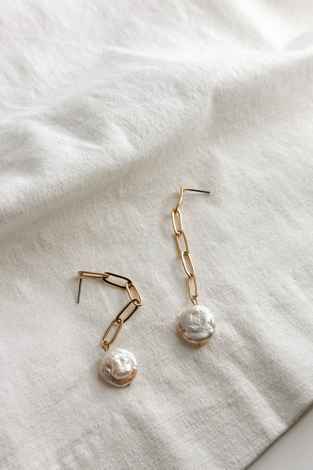 Flat lay view of the Layla Gold Chain & Flat Pearl Dangle Earring which features gold chain dangle earrings with flat pearl medallion