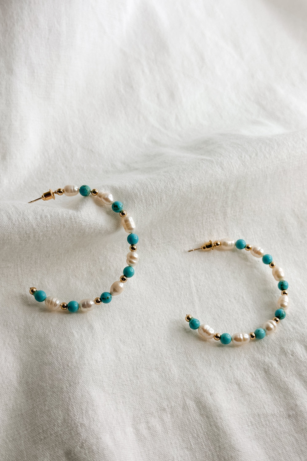 Flat lay view of the Avianna Turquoise & Pearl Hoop Earring which features large, open hoops with gold, turquoise and pearl beads