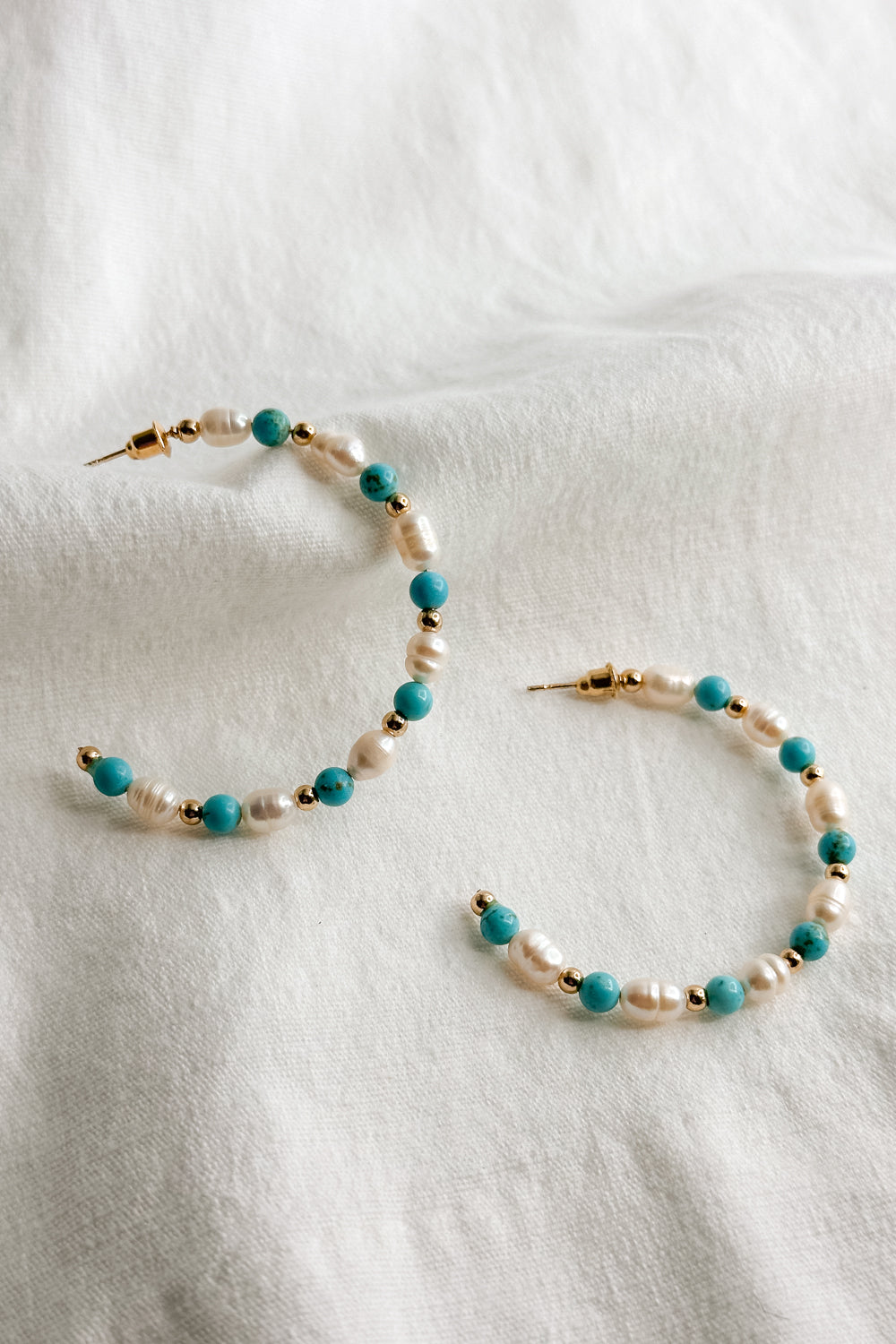 Flat lay view of the Avianna Turquoise & Pearl Hoop Earring which features  large, open hoops with gold, turquoise and pearl beads