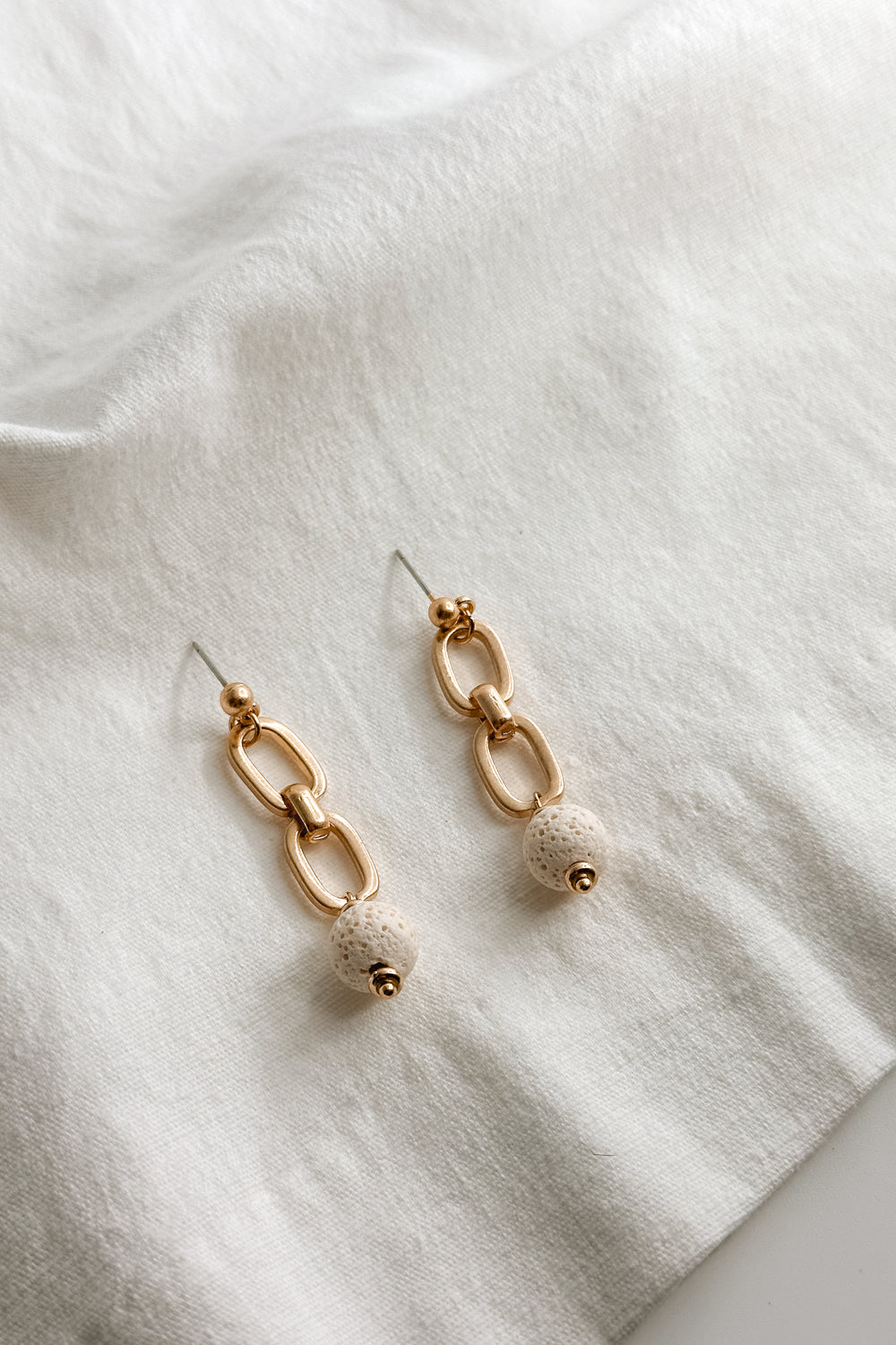 FLat lay view of the Rhodes Gold & Cream Chain Dangle Earring which features gold chain link dangle earrings with cream textured beads