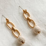 FLat lay view of the Rhodes Gold & Cream Chain Dangle Earring which features gold chain link dangle earrings with cream textured beads
