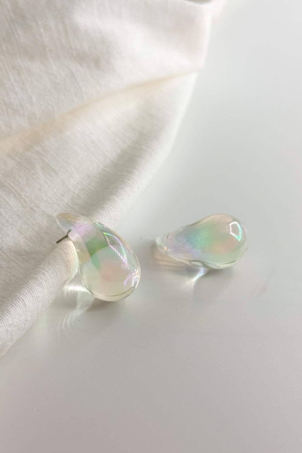 Flat lay view of the Mila Iridescent Scoop Teardrop Stud Earring which features iridescent teardrop studs
