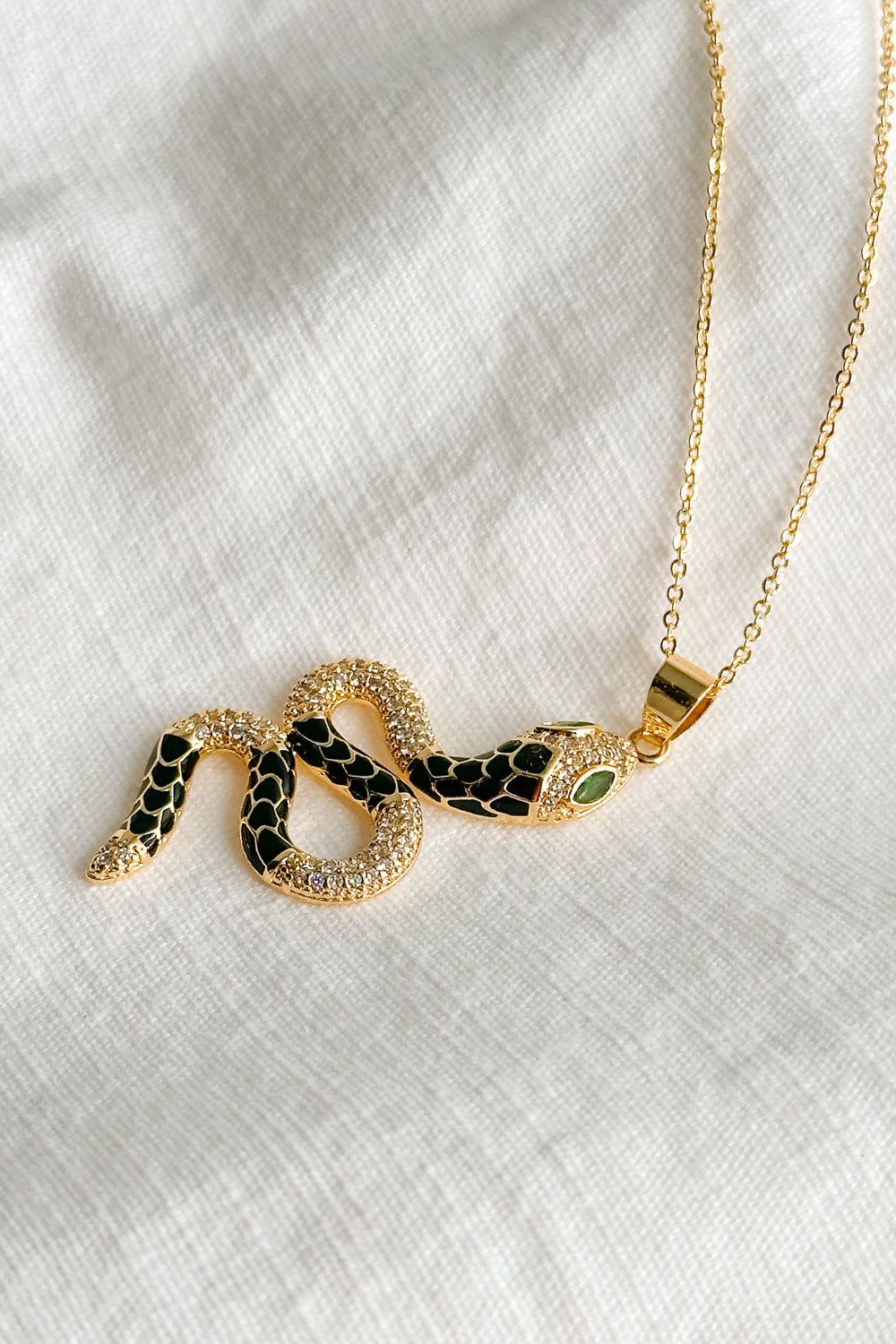 Flat lay view of the Lucia Black & Gold Snake Necklace which features gold chain link single layer with a black and gold snake medallion