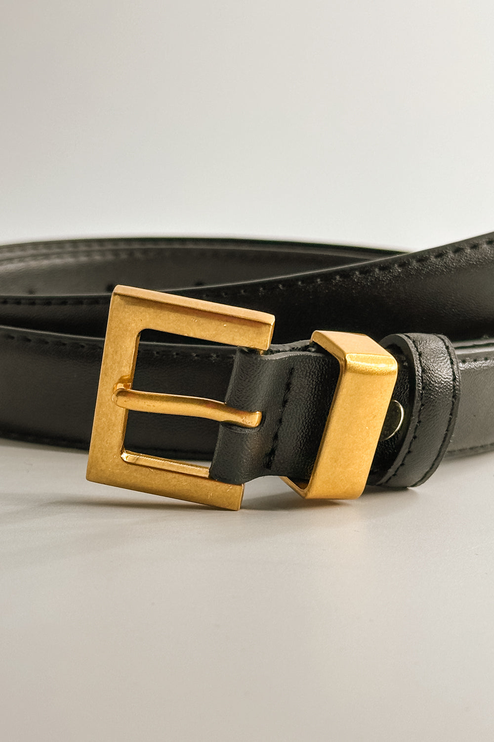 Close up view of female model wearing the Ariana Black Slim Square Buckle Belt which features Black Leather Fabric and Gold Square Adjustable Buckle