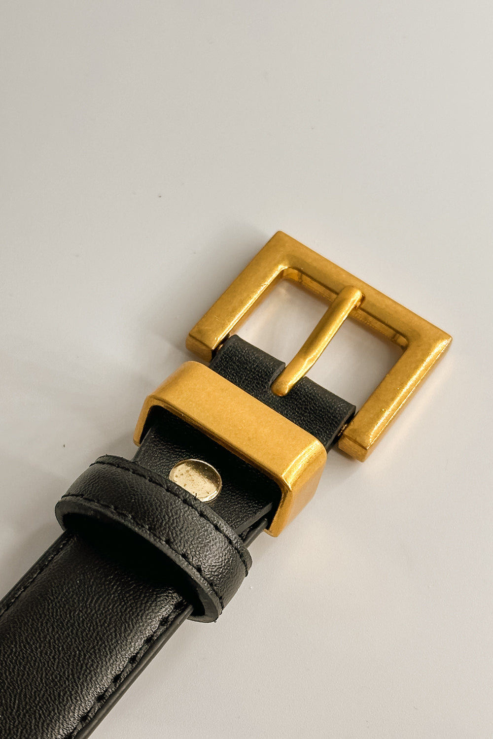 Close up view of female model wearing the Ariana Black Slim Square Buckle Belt which features  Black Leather Fabric  and Gold Square Adjustable Buckle