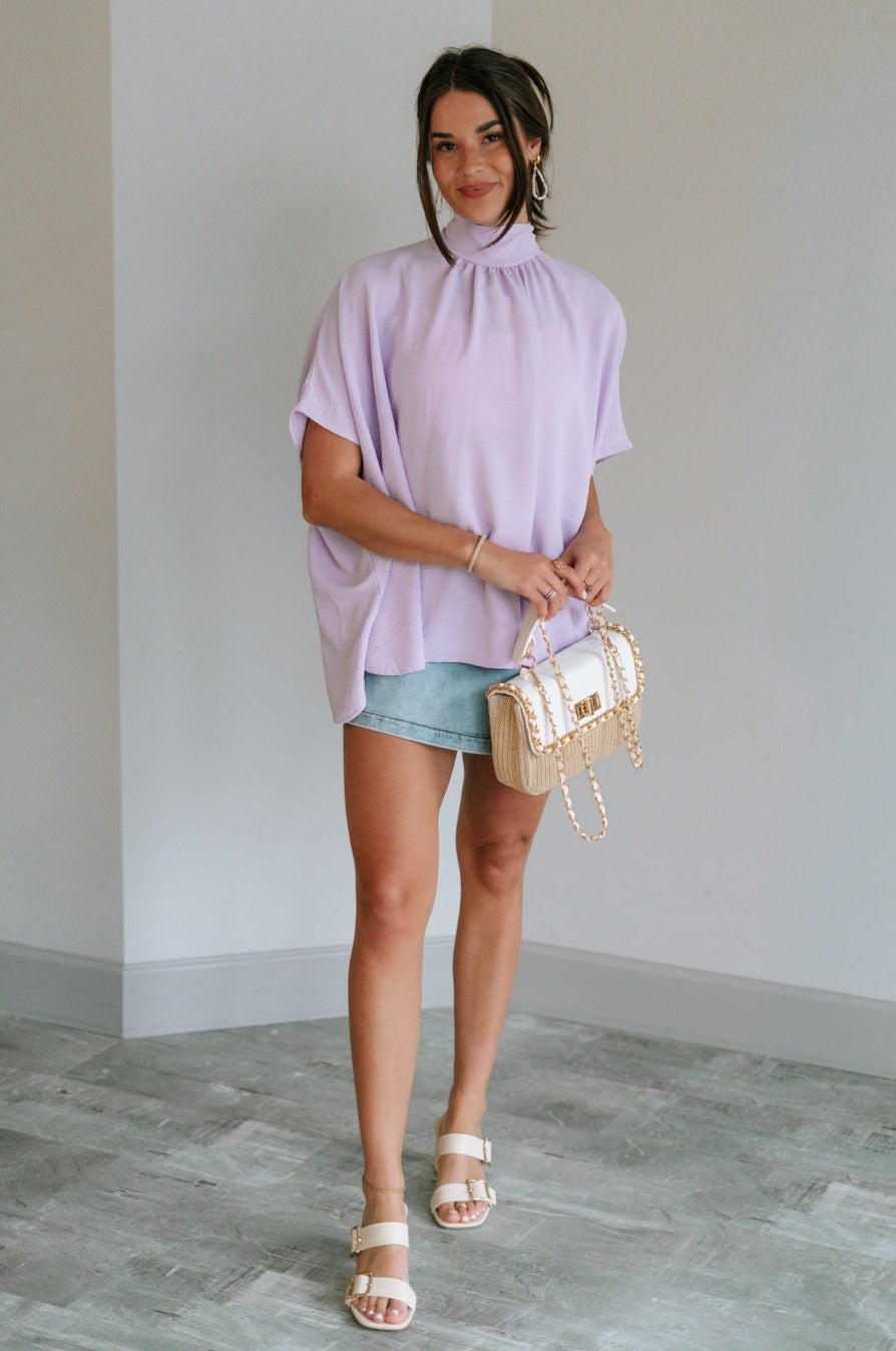 Full body view of female model wearing the Madilyn Lavender High Neck Top which features Lavender Lightweight Fabric, High Neckline with Tie Closure and Short Sleeves