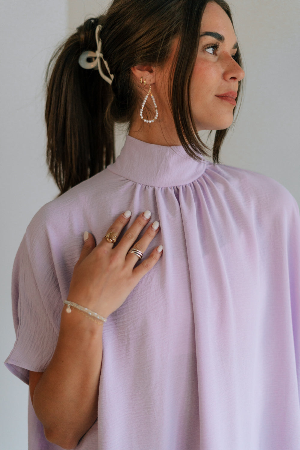 Close up view of female model wearing the Madilyn Lavender High Neck Top which features Lavender Lightweight Fabric, High Neckline with Tie Closure and Short Sleeves