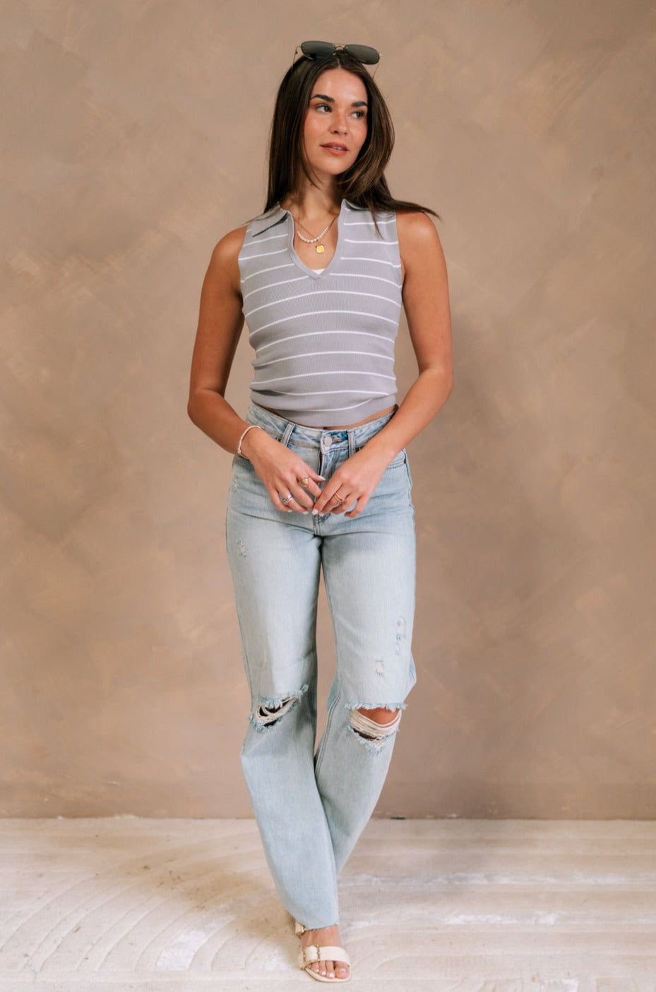 Full body front view of female model wearing the Amanda Light Wash Distressed Jeans that have light wash denim, distressing, a high waist, and wide straight legs. Worn with gray top.