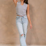 Full body front view of female model wearing the Amanda Light Wash Distressed Jeans that have light wash denim, distressing, a high waist, and wide straight legs. Worn with gray top. Model has legs crossed.