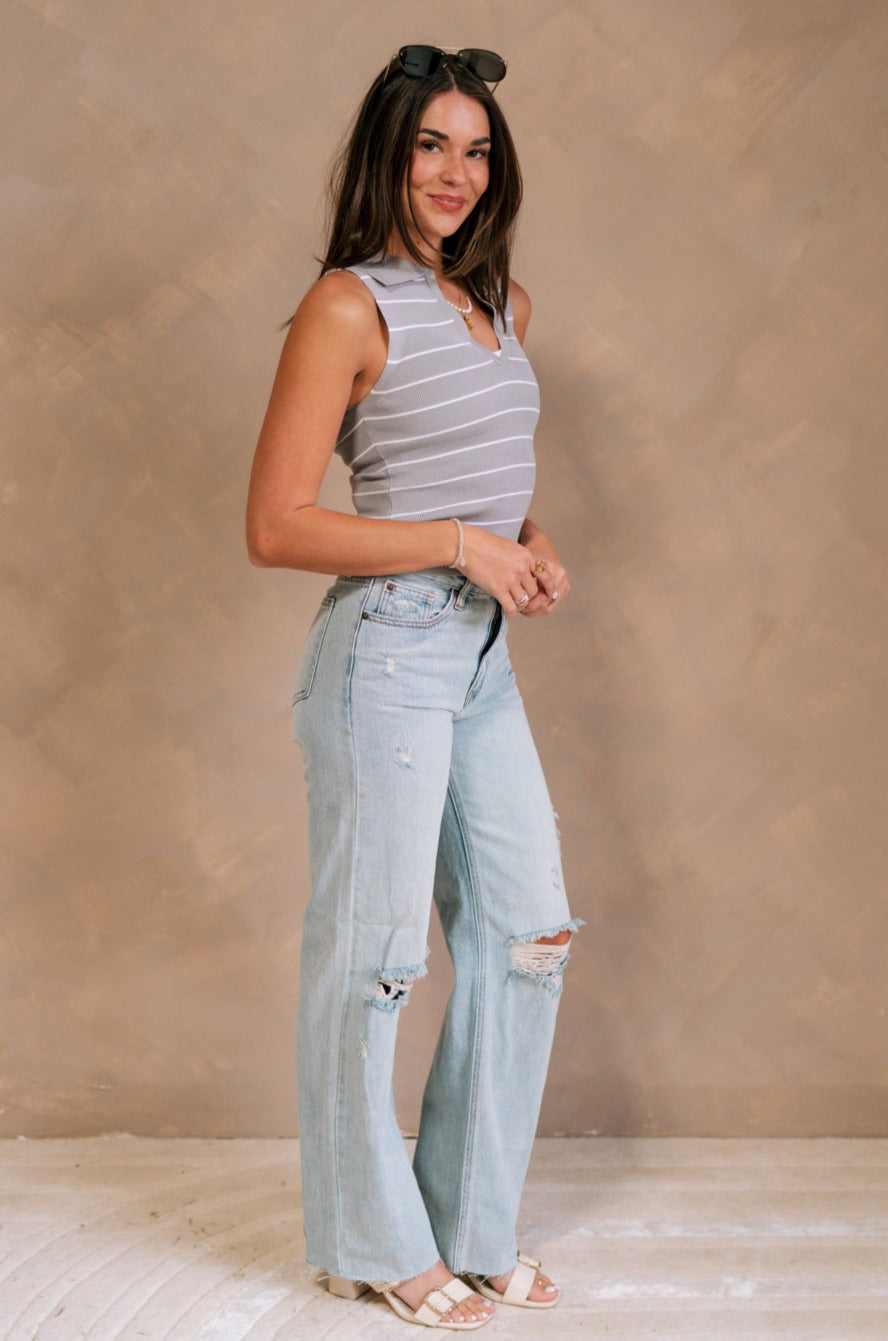 Full body side view of female model wearing the Amanda Light Wash Distressed Jeans that have light wash denim, distressing, a high waist, and wide straight legs. Worn with gray top.