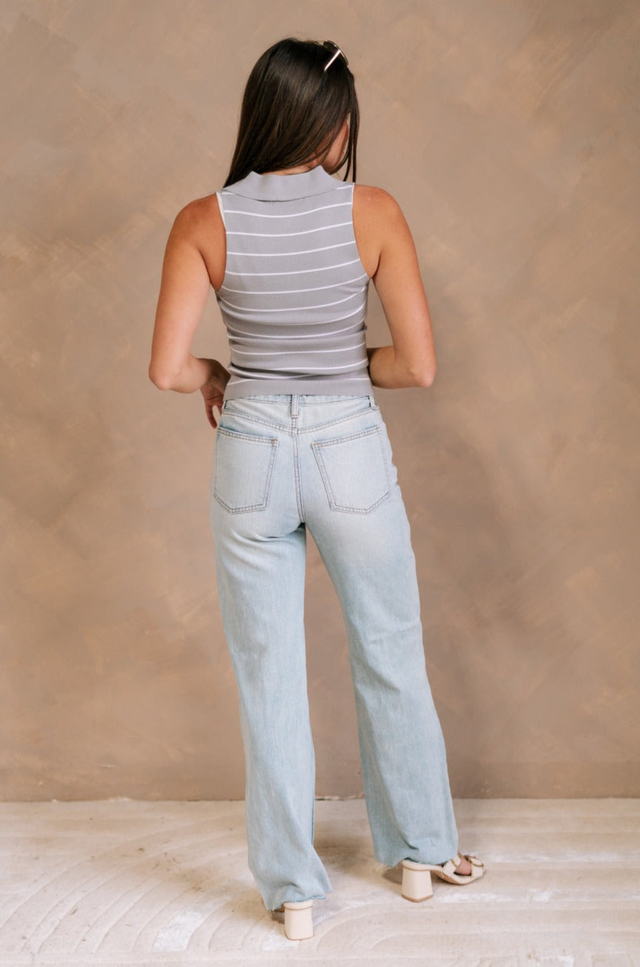 Full body back view of female model wearing the Amanda Light Wash Distressed Jeans that have light wash denim, distressing, a high waist, and wide straight legs. Worn with gray top.