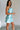 Side view of female model wearing the Dorit Light Blue Satin Mini Dress which features Light Blue Shimmer Fabric, Mini Length, Cowl Neckline and Skinny Straps