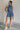 Full body view of female model wearing the Leila Dark Blue Halter Neckline Romper which features Grey Blue Textured Fabric, Two Side Slit Pockets, Halter Neckline with Tie,  Elastic Waistband and Back Key Hole