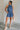 Full body view of female model wearing the Leila Dark Blue Halter Neckline Romper which features Grey Blue Textured Fabric, Two Side Slit Pockets, Halter Neckline with Tie,  Elastic Waistband and Back Key Hole