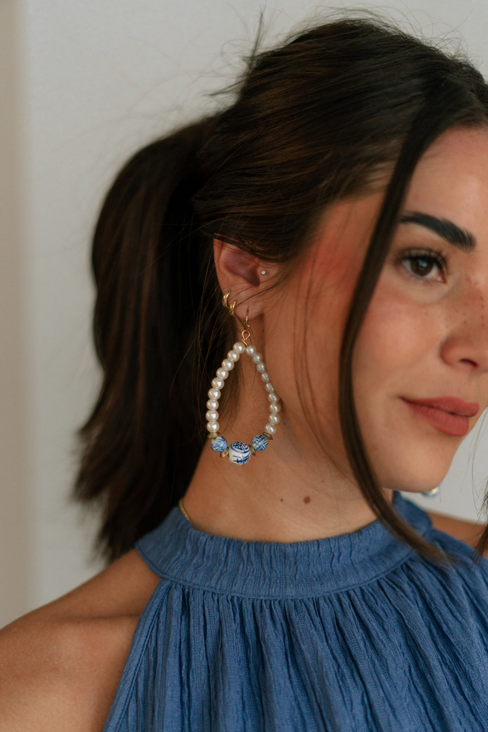 SIde view of female model wearing the Sienna White & Blue Pearl Dangle Earring which features teardrop, dangle earrings with white pearls and blue design beads
