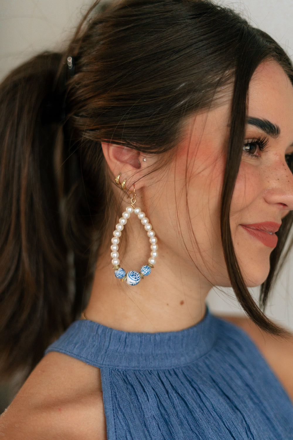 SIde view of female model wearing the Sienna White & Blue Pearl Dangle Earring which features  teardrop, dangle earrings with white pearls and blue design beads